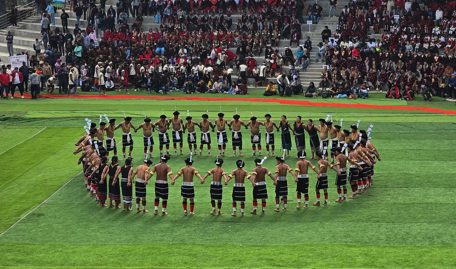 Naga dancers form a large circle on the green arena at Hornbill Festival in Kisama